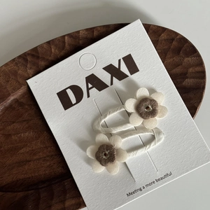 Détail de barrettes à fleurs en tissu crème et marron sur un plateau de présentation