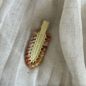Detailed top view of handmade woolen woven hair clip on natural linen fabric surface