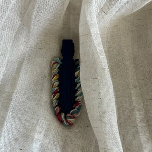 Detailed close-up of a handmade woven hair clip with colorful wool on a beige linen base