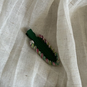 Detailed view of dark green hair clip with colorful woven texture on soft fabric background