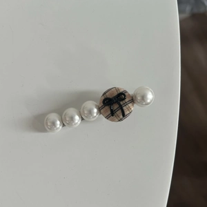 Detailed view of hair clip with faux pearls and brown check pattern fabric button