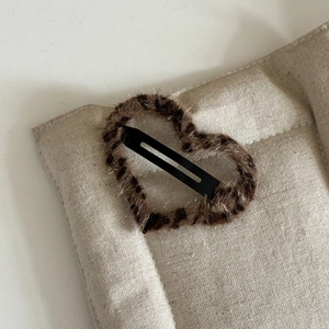 Macro shot of heart-shaped leopard print plush hair clip on beige linen background texture