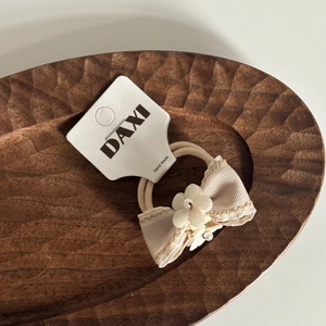 Détail d'un élastique à cheveux nœud crème fait main avec perle sur plateau bois