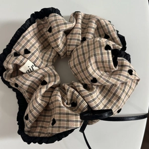 Detail of beige plaid scrunchie with black heart pattern and ruffled ribbon trim