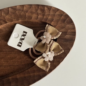 Détail d'un élastique à cheveux marron avec nœud, dentelle et perle sur carte support
