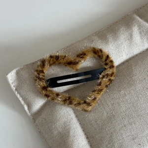 Close-up of heart-shaped leopard print plush hair clip on a beige fabric background
