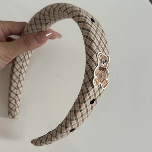 Close-up of padded beige plaid headband with cute embroidered bear patch detail