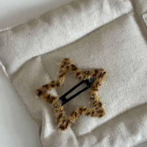 Detailed view of a plush leopard print star-shaped hair clip with a sturdy metal snap base