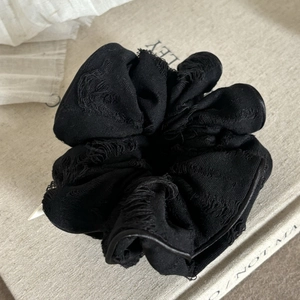 Detailed close-up of a large black textured scrunchie with distressed fringe edges
