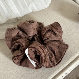 Close-up of textured dark brown scrunchie with detailed stitching on a fabric surface