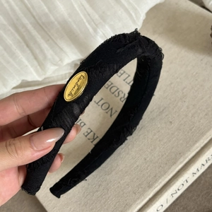 Close-up of a distressed black fabric headband with a gold handmade metal plate detail