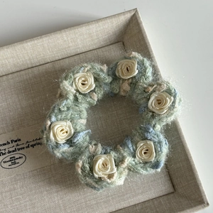 Close-up of handmade crochet hair tie with white satin roses on green knit fabric
