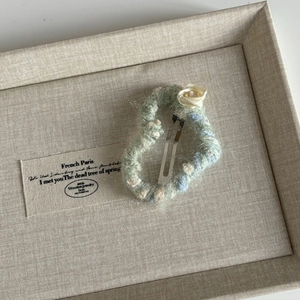 Close-up of a handmade knit hair clip with a cream satin rose and silver metal base