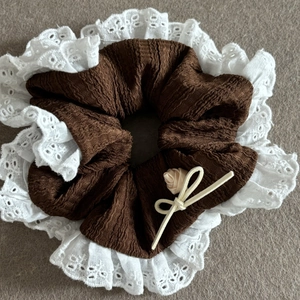 Close-up of brown crinkled fabric scrunchie with white eyelet lace and apricot rose