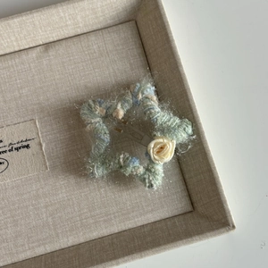 Detail of star-shaped knitted hair clip with cream ribbon rose on green yarn background