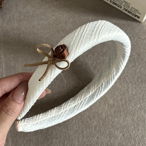 Close-up of white wavy fabric headband with a brown satin rose and bow detail