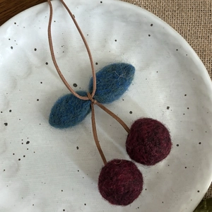 Détail d'un pendentif cerise en feutre de laine fait main avec boules rouges et feuilles