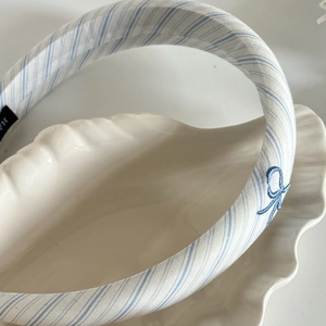 Detail of blue striped headband with bow embroidery on white decorative shell tray