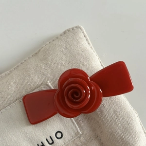 Elegant red rose acetate flower hair clip on textured beige linen background