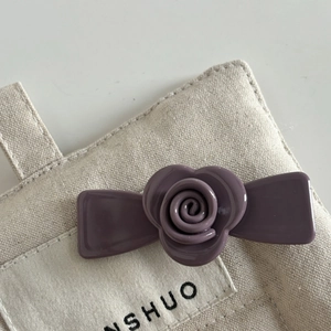 Detailed view of a deep purple rose acetate hair clip on a minimalist canvas bag background