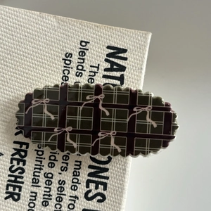 Detail of oval hair clip featuring green plaid pattern and pink bow prints with wavy edges
