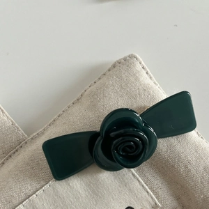 Close-up of a dark green resin camellia hair clip styled on a beige canvas bag