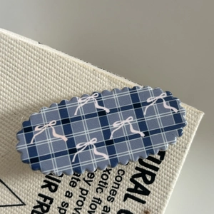 Detailed view of blue plaid acrylic hair clip with pink ribbon bow and scalloped edges