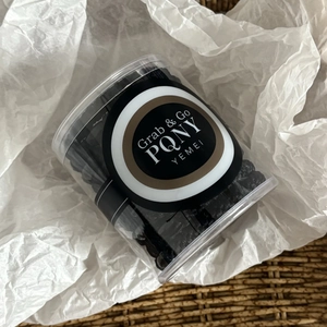 Elastic black hair ties set in a clear jar on white textured fabric for ponytail styling