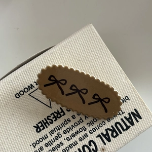 Brown oval hair clip with black bow patterns and wavy edges on a white gift box
