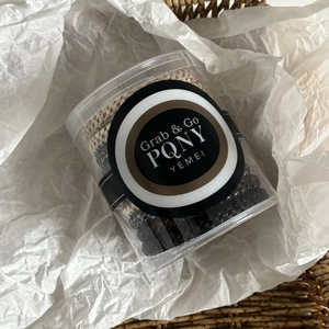 Detail of woven elastic hair ties in neutral tones stored in a clear cylinder container
