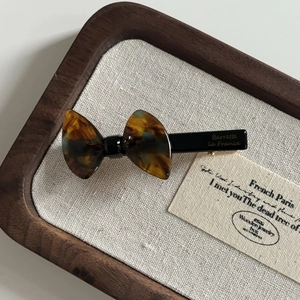 Detailed view of a tortoise shell bow hair clip with gold logo on dark wood tray