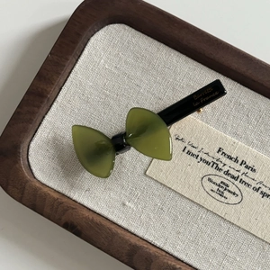 Detailed macro view of dark green acetate bow hair clip with gold text on walnut wood tray