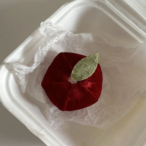 Macro shot of red velvet apple hair clip with green leaf detail in gift box packaging