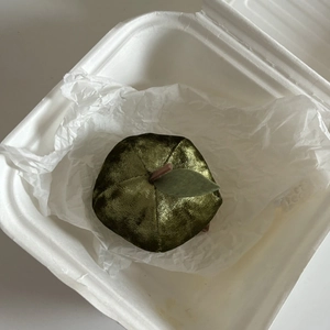 Detailed top view of a velvet apple hair claw in olive green placed in a white gift box