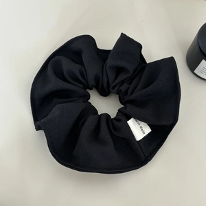 Macro detail of black fabric scrunchie texture with a white Hand Made sewn label