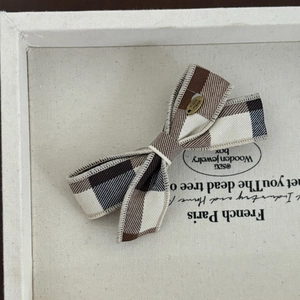 Handmade brown plaid bow hair clip with vintage golden metal label on white tray