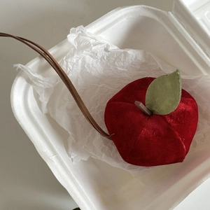 Detail shot of a red velvet apple charm with green leaves in a white container