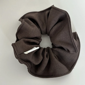 Detailed view of coffee brown scrunchie with ribbed fabric texture and white brand label