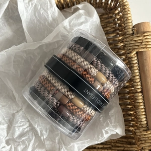 Detail showing elastic hair ties in neutral earth tones inside a clear storage cylinder