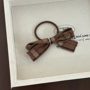 Detail of handmade brown plaid bow hair tie with engraved gold metal charm