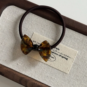 Brown tortoiseshell resin bow hair tie with dark brown elastic band on decorative tray