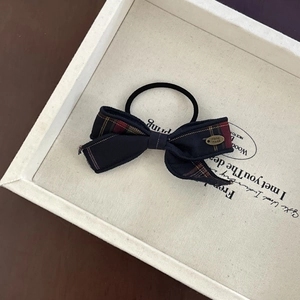 Close-up of a red and black plaid bow hair tie with a vintage gold Handmade metal tag