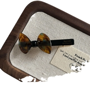 French tortoise shell acetate bow hair clip with gold logo on a rustic linen tray