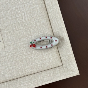Macro detail of white enamel hair clip with red polka dots and cherry rhinestone decor