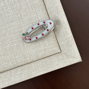 Detailed view of an oval polka dot hair clip with sparkling cherry rhinestone accents