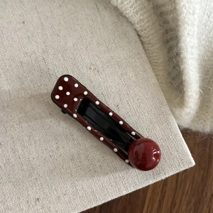Close-up of vintage red polka dot hair clip with glossy bead on a textured fabric base