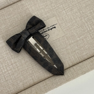 Close-up of a dark grey bow hair clip with denim texture and silver metal fastener