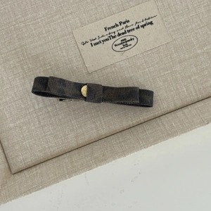 Detail of dark charcoal bow hair clip with gold metal center on a beige textile background