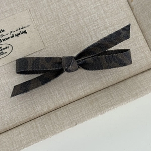 Detail of a dark leopard print bow hair clip with textured denim fabric on linen background