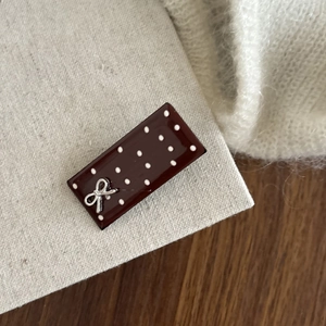 Detailed view of a vintage brown polka dot hair clip with a silver bow on a beige card